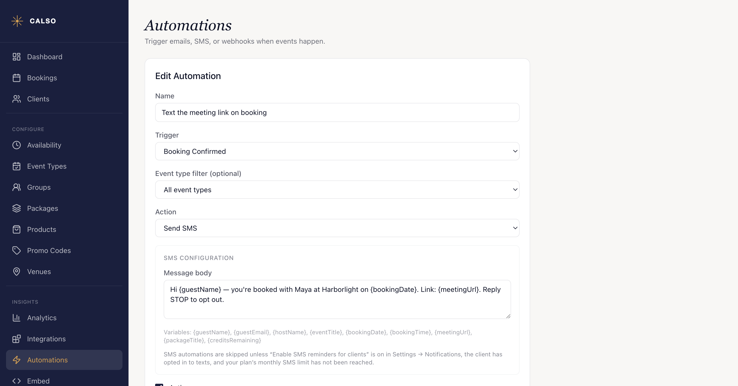 The automation editor with a Booking Confirmed trigger and a Send SMS action, its Message body carrying the variables in curly braces — {guestName}, {bookingDate} and {meetingUrl} — exactly as typed, with the grey hint beneath the field listing all nine variables and the conditions under which an SMS automation is skipped.